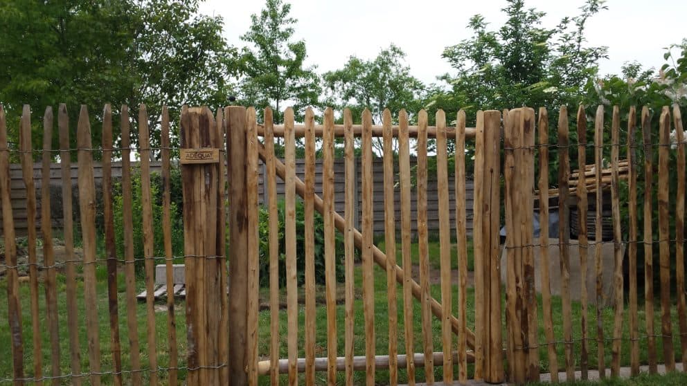 Franse rondhoutpoort van 120 cm hoog met rondhoutpoort van 120 cm hoog bevestigd aan schapenhek als afrastering en doorgaan naar een deel van een tuin