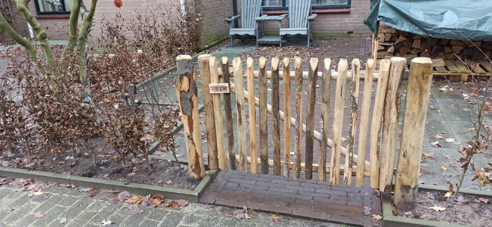 Franse rondhoutpoort van kastanje van 80 cm hoog bij 120 cm breed als doorgang gebruikt in een voortuin.