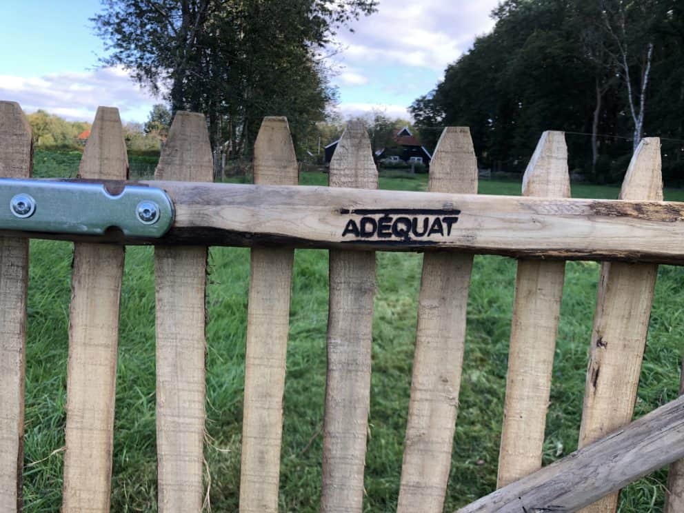 Franse rondhoutpoort van kastanjehout 120 cm hoog met het logo van Adéquat erin gebrand.