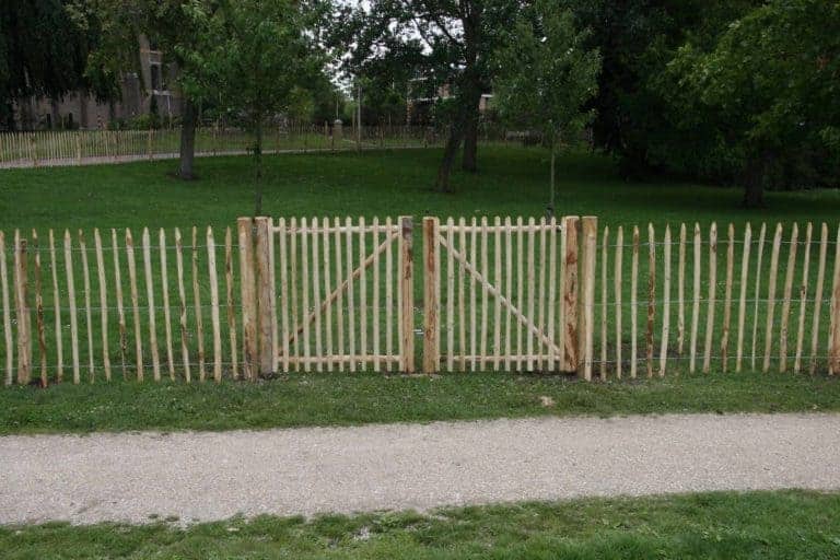 Dubbele Franse rondhoutpoort van 100 cm hoog als doorgang bij een omheining van schapenhek van 100 cm hoog met een latafstand van 8 cm.