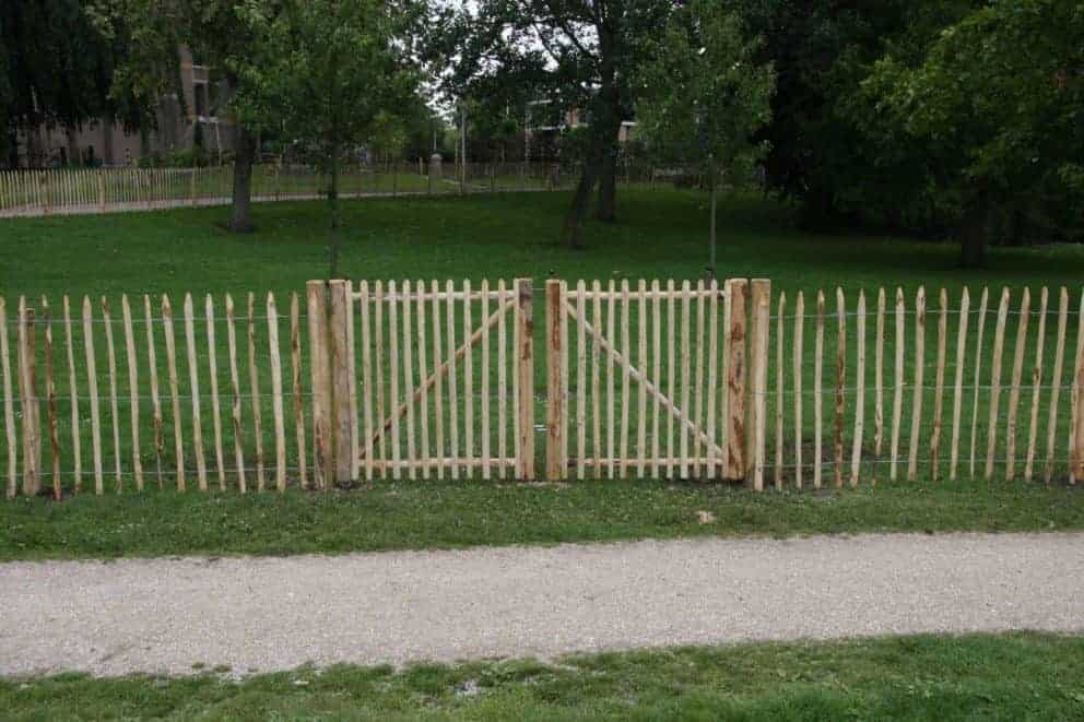 Dubbele Franse rondhoutpoort van 100 cm hoog als doorgang bij een omheining van schapenhek van 100 cm hoog met een latafstand van 8 cm.