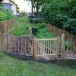 Franse Franse rondhoutpoort van 80 cm hoog en 100 cm breed gebruikt als doorgang naar een moestuin die omheind is door schapenhek van 80 cm hoog