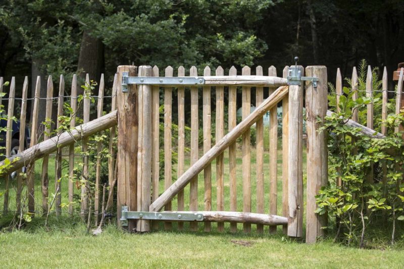 Franse rondhoutpoort van 100 cm hoog geplaatst in een groene tuin tussen schapenhek met dezelfde afmeting.