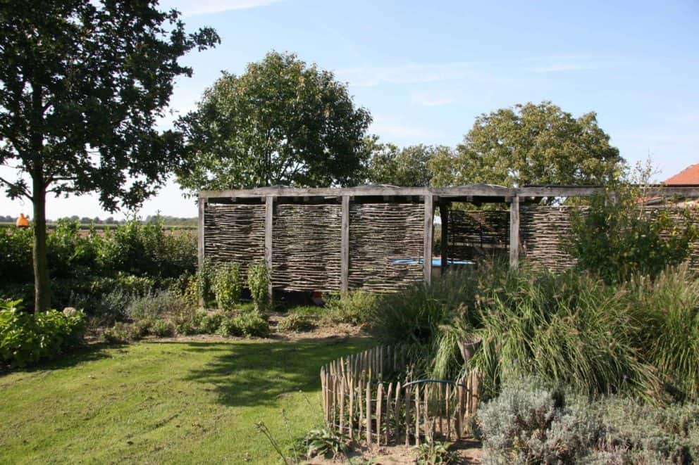 Hazelaarscherm Somme 1 gebruikt als creatieve afrastering in een tuin. De schermen zijn geplaatst tussen een houten balken constructie.