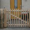 Franse rondhoutpoort van 80 cm hoog tussen schapenhek van dezelfde afmeting als afrastering en doorgang naar de voortuin bij een huis.