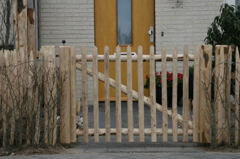 Franse rondhoutpoort van 80 cm hoog tussen schapenhek van dezelfde afmeting als afrastering en doorgang naar de voortuin bij een huis.