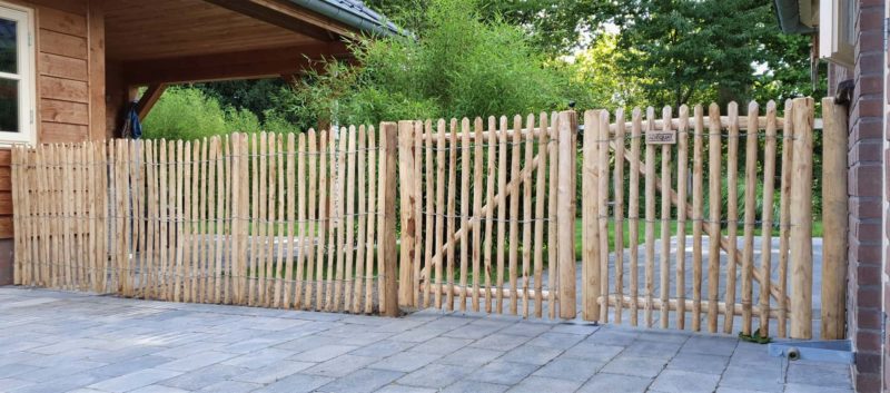 Rasterscherm van 100 cm hoog met latafstand 2 cm tussen twee gebouwen en aan een dubbele raamwerkpoort bevestigd met dezelfde hoogte.