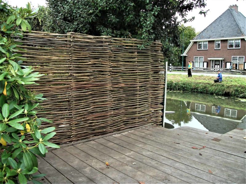 Gevlochten wilgentenen scherm als afrastering van de tuin. de wilgenten zijn geplaatst bij het water in iemand zijn tuin.