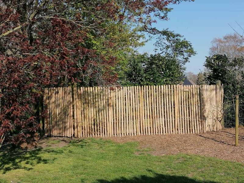 Rasterscherm van halfronde latten 150 cm hoog met latafstand 2 cm met een poort bekleed met hetzelfde rasterscherm.