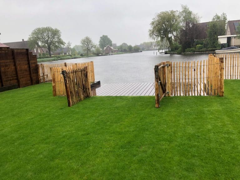 Franse dubbele rondhoutpoort van 100 cm hoog als doorgang naar het meer aan de tuin. De Franse robdnhoutpoort staat tussen een schapenhek omheining van 100 cm hoog met een latafstand van 4 cm