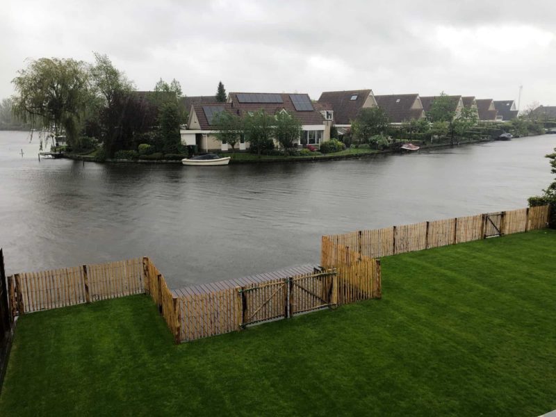 Franse dubbele rondhoutpoort van 100 cm hoog als doorgang naar het meer aan de tuin. De Franse robdnhoutpoort staat tussen een schapenhek omheining van 100 cm hoog met een latafstand van 4 cm