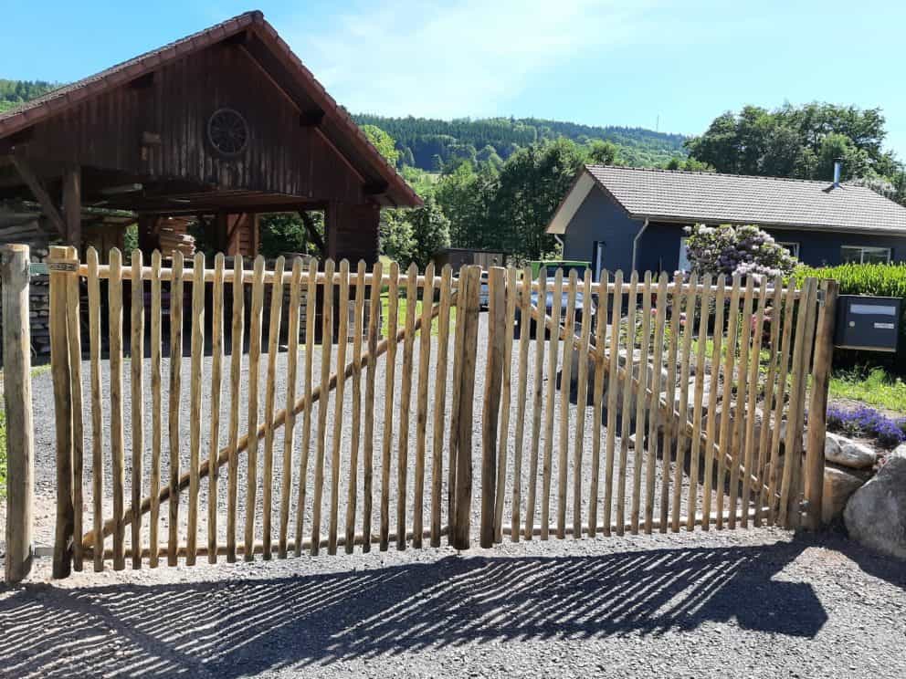 Dubbele Franse rondhoutpoort als doorgang naar een woonerf in een groenrijke omgeving