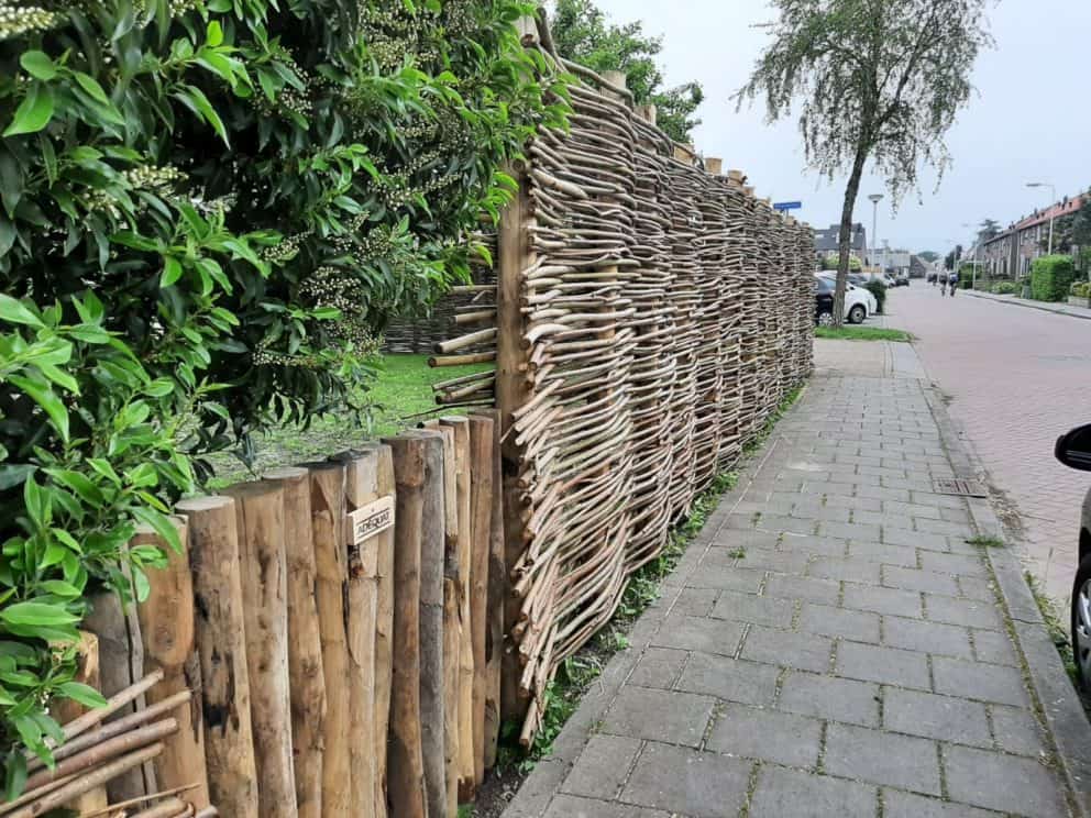 Wilgentenen schutting in combinatie met kastanjehouten palen van 7 - 9 cm. De schutting staat in de voortuin aan de kant van de weg aan het stenen voetgangerspad van de straat.