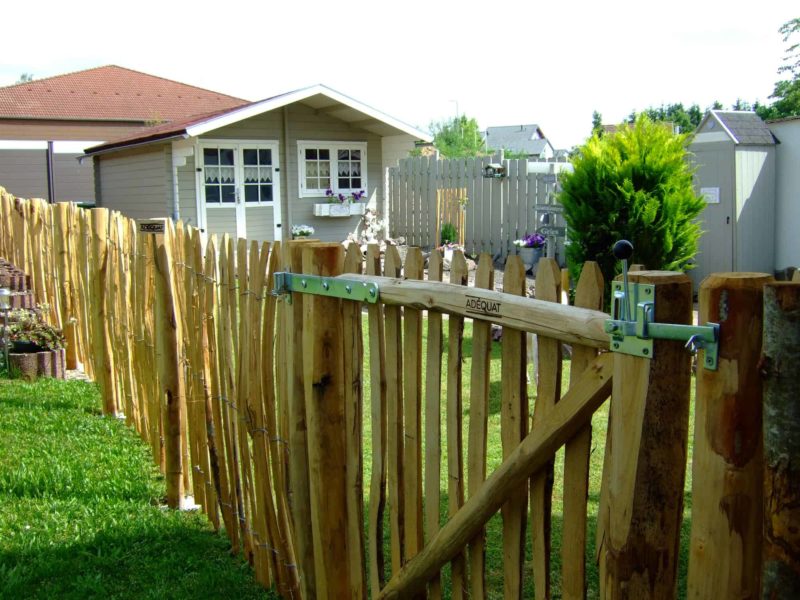 Franse rondhoutpoort van 120 cm breed bij 120 cm hoog bevestigd aan schapenhek van 120 cm hoog met een latafstand van 4 cm als afscheiding in een tuin.