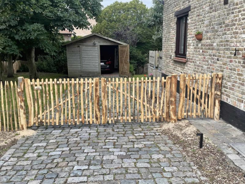 Dubbele franse rondhoutpoort van 150 cm breed bij 100 cm hoog per poortdeel en een looppoortje van 80 cm breed bij 100 cm hoog als doorgang naar een carpoort