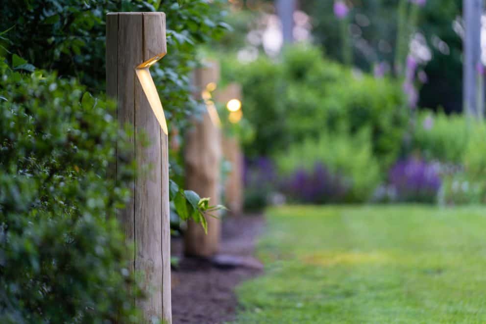 Rond houten tuinverlichting Billy op een rij in tuin met veel bloemen