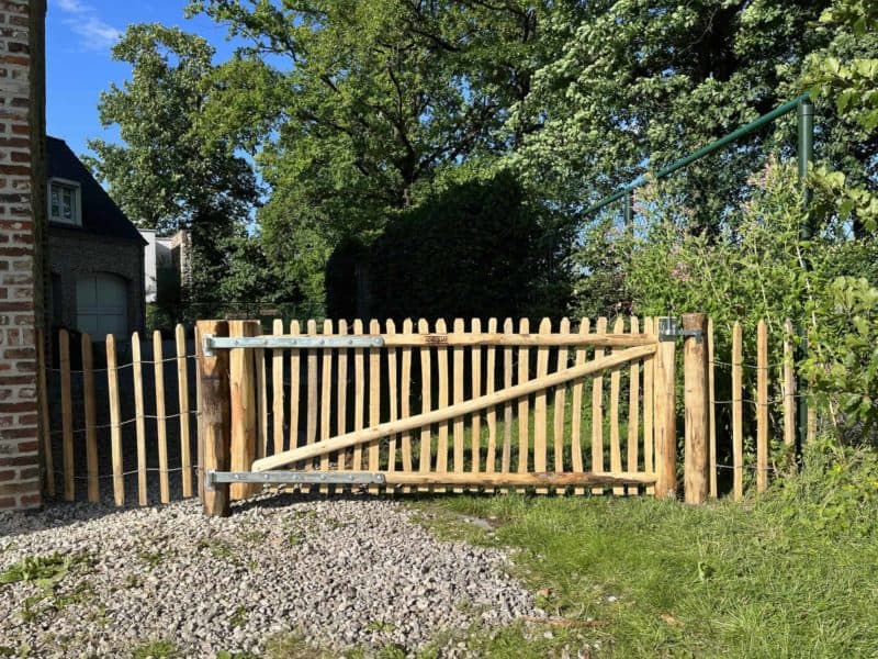 Franse rondhoutpoort van 80 cm hoog en 200 cm breed als toegang tussen een huis en de heg.