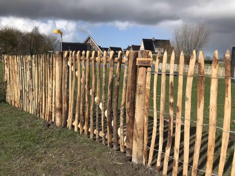 Kastanje rondhoutpoort van 100 cm hoog en 120 cm breed als toegang naar een weide geplaatst tussen schapenhek van 100 cm hoog met een latafstand van 4 cm.