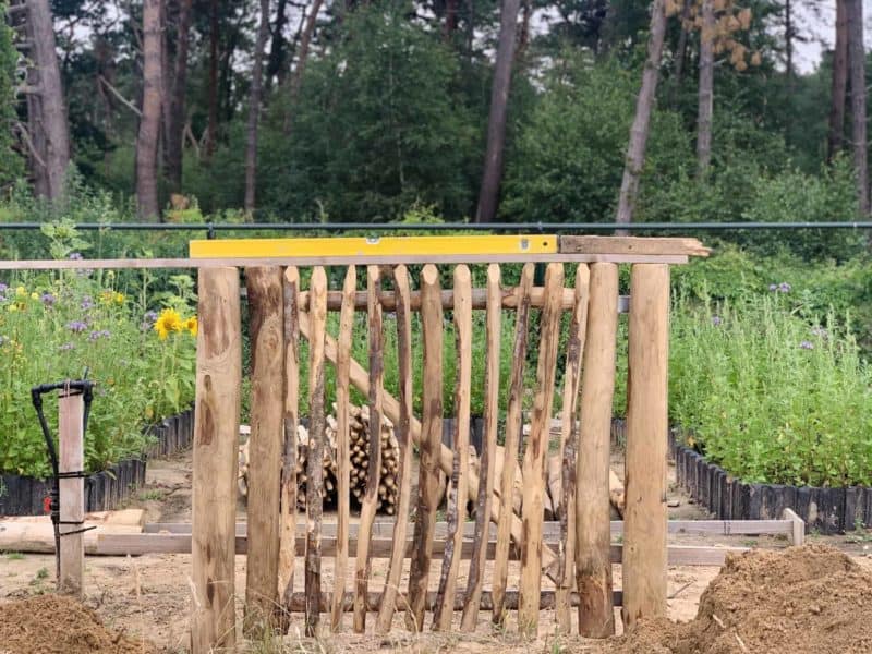 Franse rondhoutpoort van 100 cm breed bij 100 cm hoog die net geplaatst wordt met een waterpas erop.