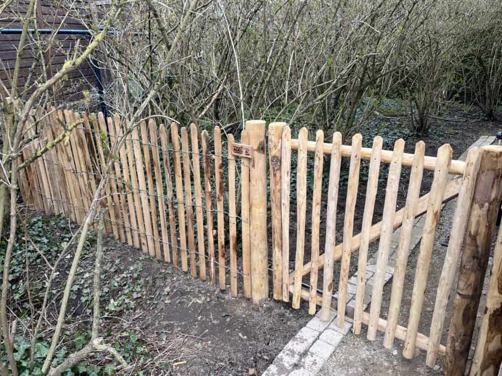 Robinia schapenhek 100 cm hoog, latafstand 4 cm en een Franse rondhoutpoort 100 cm hoog bij 100 cm breed als toegang in een tuin.