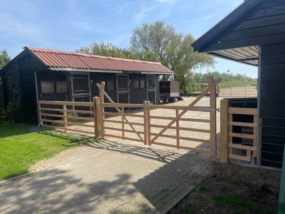 Op de foto staat een dubbele engelse douglas toegangspoort van 180 cm breed en 120 cm hoog. De poort staat tussen twee paarden schuren in en dient als afscheiding van de tuin en de paardenwei.