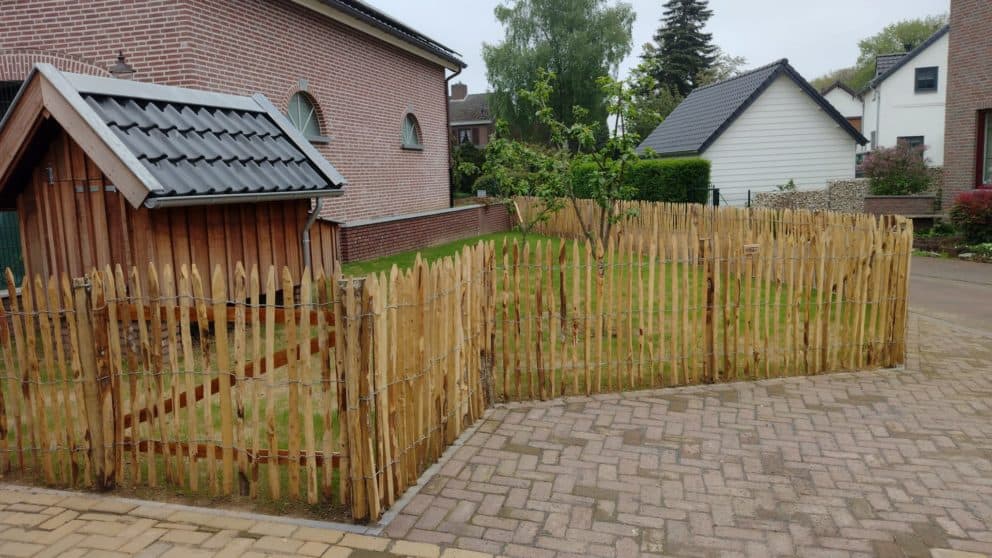 Hekwerk van 100 cm hoog en latafsstand 4 cm. Dit schapenhek is gebruikt als afrastering voor een kippenhok. Het kippenhok staat aan de linker kant van de foto en in het midden een kleine boom. Daaromheen staat de omheining. De kippen omheining staat vast aan de woning.