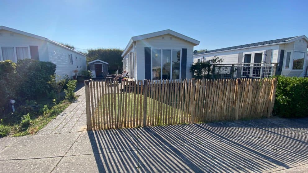 Frans schapenhek van 120 cm hoog met een latafstand van 2 cm gebruikt als afscheiding bij een chalet. De foto is van voren genomen waarbij je uitkijkt op het hekwerk en de chalet. Zowel rechts als links staat nog ee chalet.