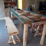 Boomstambankje van kastanjehout van 150 cm breed en twee kastanjehouten krukjes. Deze staan bij een tafel binnen in de woning. De bankjes en de tafel stralen een Ibiza look uit.