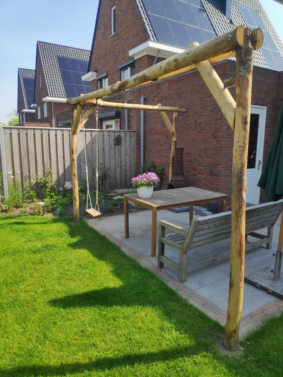 Een pergola van ronde en halfronde kastanjehhouten palen met een diameter van 10 - 12 cm in verschillende lengtes. Aan de pergola is aan de linker kant een schommel bevestigd.