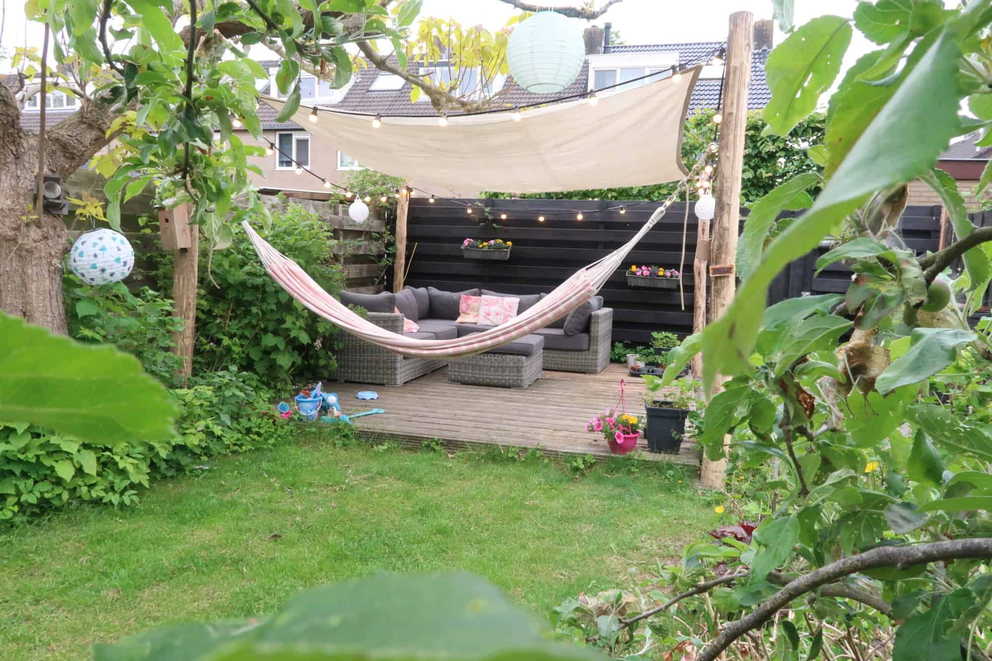 Geschilde en geschuurde robinia palen met een diameter van 12 - 14 cm gebruikt voor het maken van een constructie voor een zonnendoek en een hangmat. Deze palen staan in de tuin in een hoekje bij de schutting. Aan de palen is een zonnedoek en een hangmat bevestigd. Onder de zonnedoek staat een loungeset.