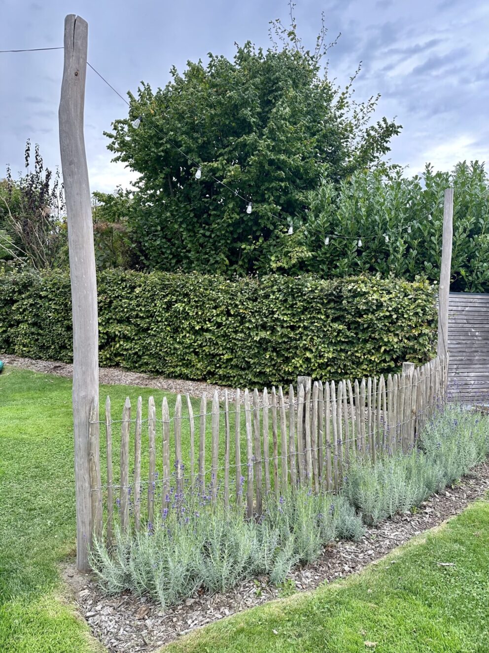 Omheining bij speeltuin gemaakt van Frans schapenhek 100 cm hoog, latafstand 4 cm met robinia palen 160 en 400 cm lang, diameter 10/12 cm met een lichtsnoer eraan.