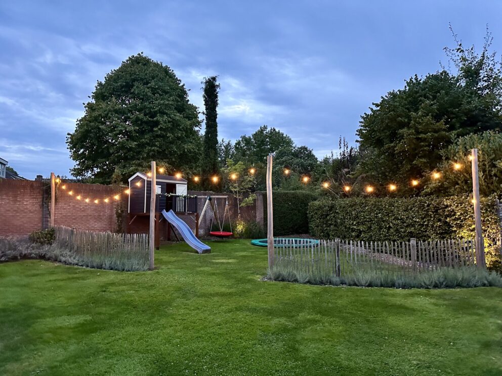 Omheining bij speeltuin gemaakt van Frans schapenhek 100 cm hoog, latafstand 4 cm met robinia palen 160 en 400 cm lang, diameter 10/12 cm met een lichtsnoer eraan.