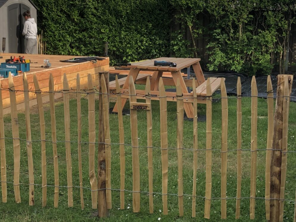 Frans schapenhek 100 cm hoog, latafstand 4 cm, 2 x 5m en kastanje paal 150/160 cm lan, diameter 7-9 cm, gepunt als afrastering in een tuin met een picknick tafel op de achtergrond