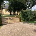 Eiken plantplaal 15 x 15 x 210 cm met diamantkop, eiken plantpaal 15 x 15 x 210 cm met diamantkop, Engelse poort trekboom eiken op maat gemaakt, 320 cm breed en 120 cm hoog, linksdraaiend. Poort bij een oprit met uitzicht op een kerk.