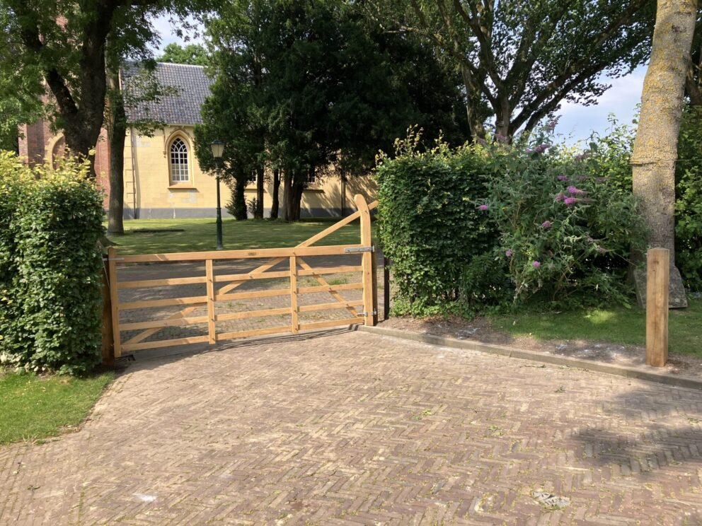 Eiken plantplaal 15 x 15 x 210 cm met diamantkop, eiken plantpaal 15 x 15 x 210 cm met diamantkop, Engelse poort trekboom eiken op maat gemaakt, 320 cm breed en 120 cm hoog, linksdraaiend. Poort bij een oprit met uitzicht op een kerk.